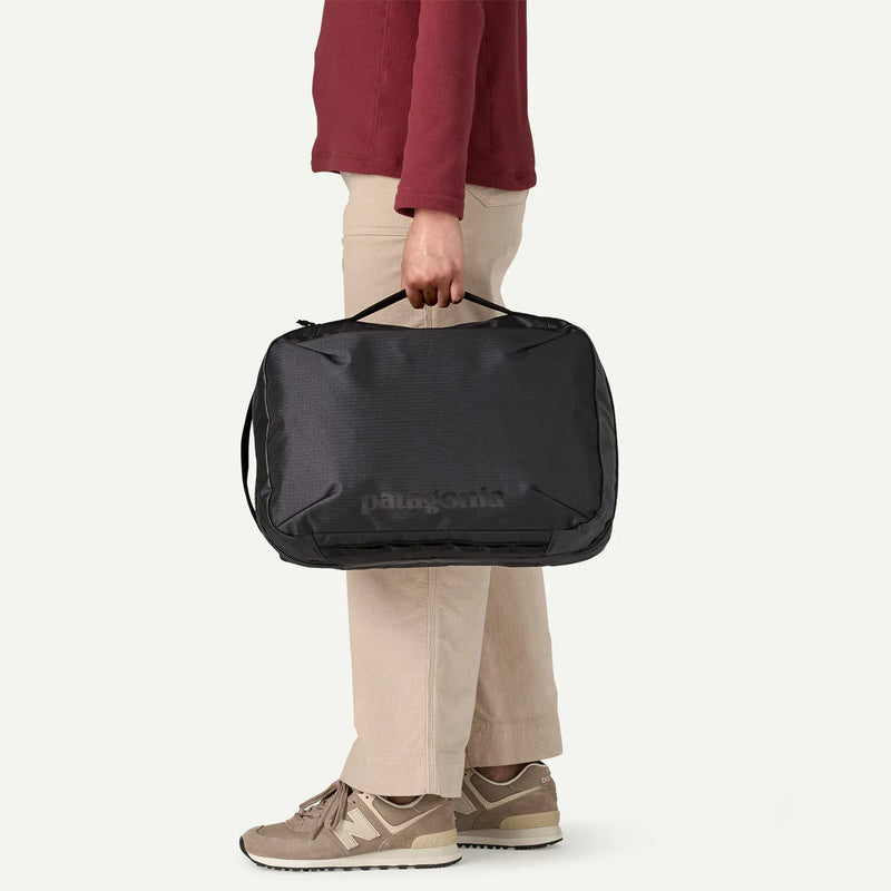 Load image into Gallery viewer, Person holding a black duffel bag with Patagonia branding on a white background