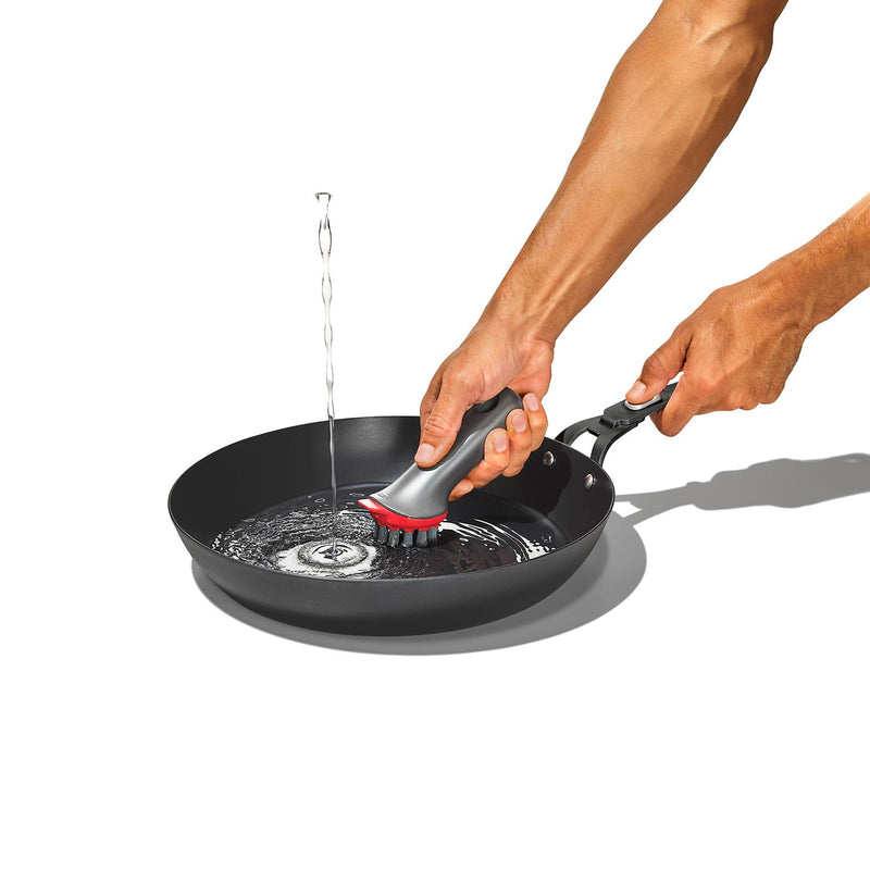 Load image into Gallery viewer, Person cleaning a black frying pan with a brush on a white background