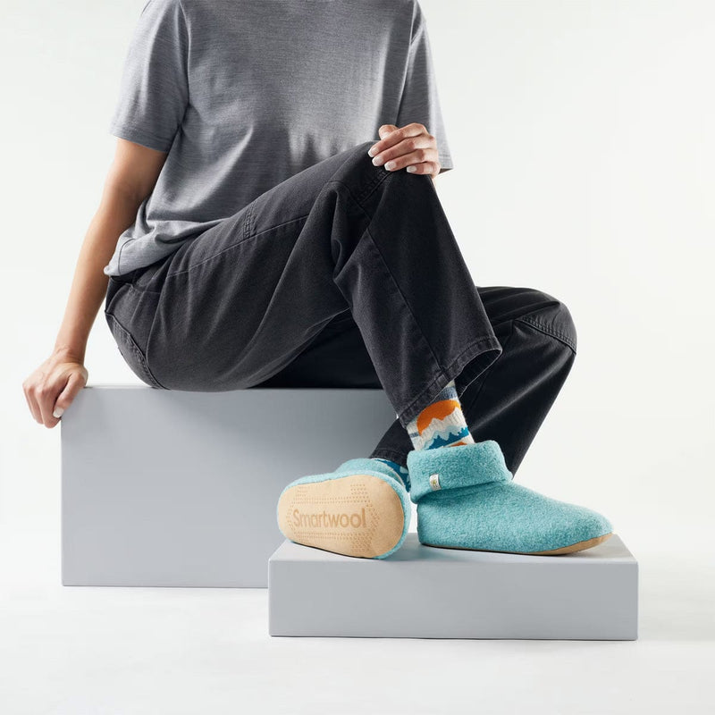 Load image into Gallery viewer, Person wearing teal Slumberfootz slippers with a visible brand logo on a white background