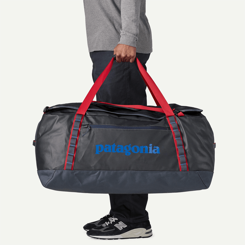 Load image into Gallery viewer, Person holding a Patagonia duffel bag with red straps on a light gray background