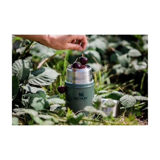 Hand placing cherries into a Stanley food jar in a natural setting