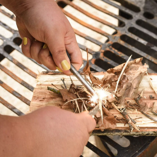 Person lighting dry leaves with a match on a grill