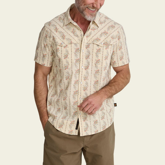 Man wearing a patterned shirt and beige pants on a plain background