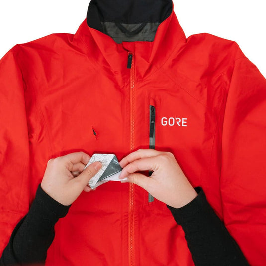 Person wearing a red jacket with 'GORE' branding, holding a card.