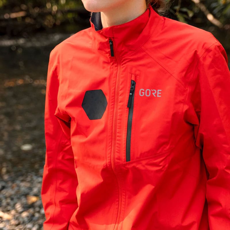 Load image into Gallery viewer, Person wearing a red jacket with GORE branding outdoors.
