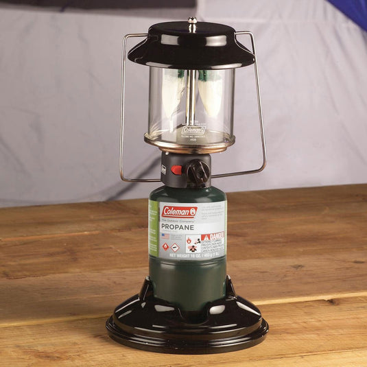 Coleman propane lantern on a wooden surface with a gray background