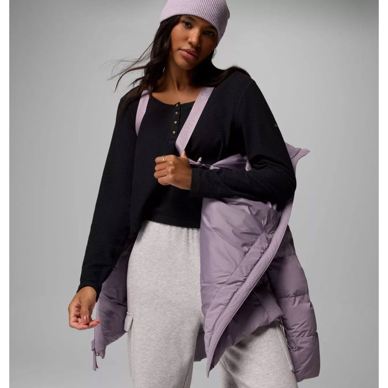 Load image into Gallery viewer, Woman wearing a black top, light gray pants, and a purple puffer jacket with a matching beanie against a gray background.
