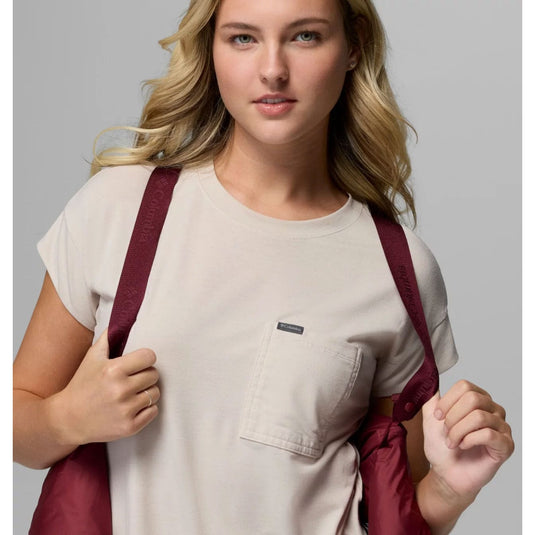 Woman wearing a beige shirt with a maroon backpack against a gray background