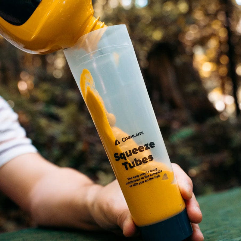 Load image into Gallery viewer, Hand filling a Coghlan's squeeze tube with yellow paint against a blurred natural background
