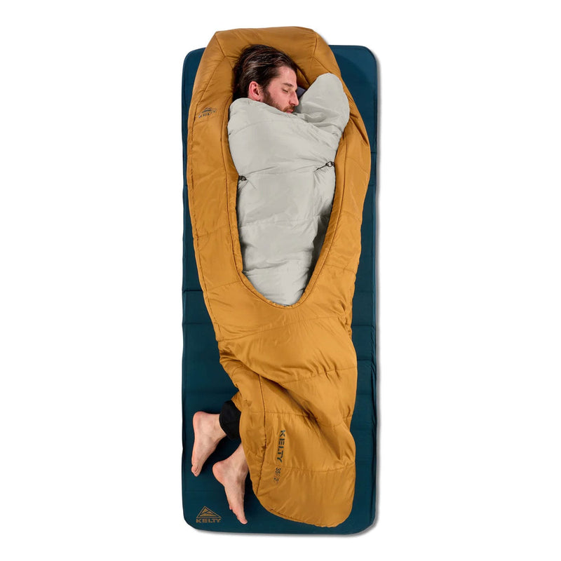 Load image into Gallery viewer, Person lying in a mustard yellow sleeping bag on a blue camping mat.
