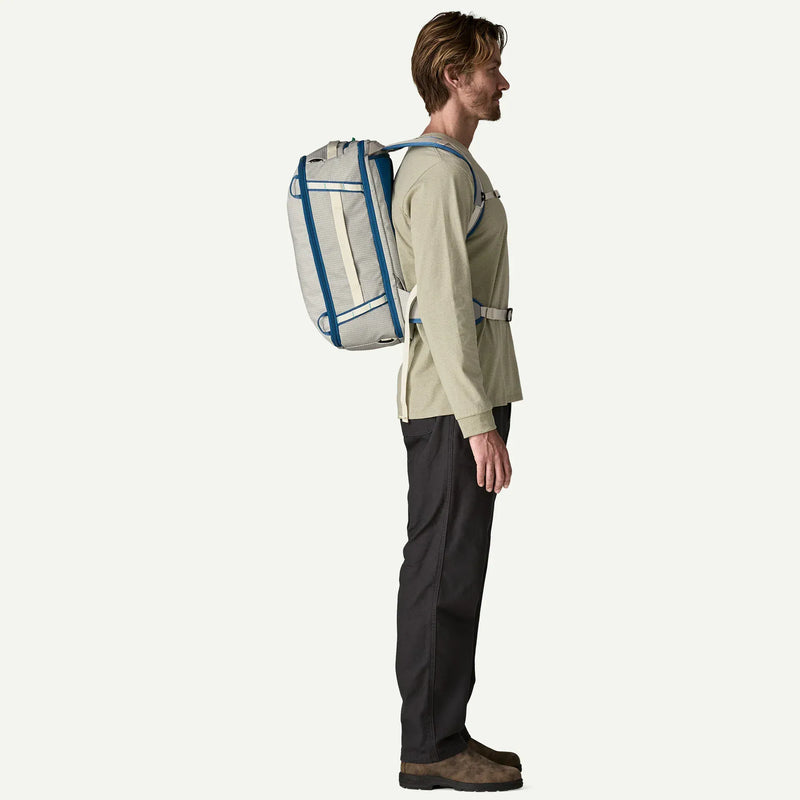 Load image into Gallery viewer, Person wearing a beige jacket and black pants with a large white backpack featuring blue accents on a white background
