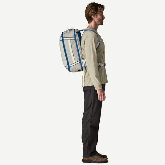 Person wearing a beige jacket and black pants with a large white backpack featuring blue accents on a white background