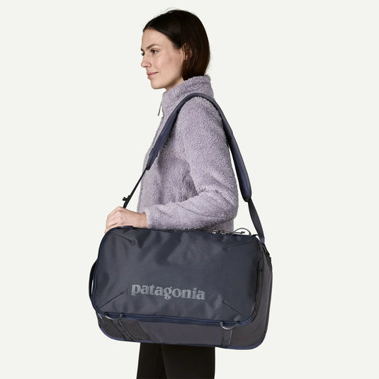 Woman carrying a navy and grey Patagonia duffel bag on a white background