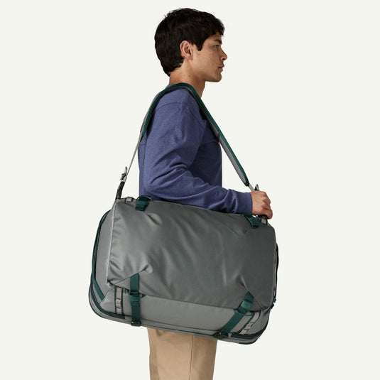 Person carrying a gray duffel bag with green straps on a white background
