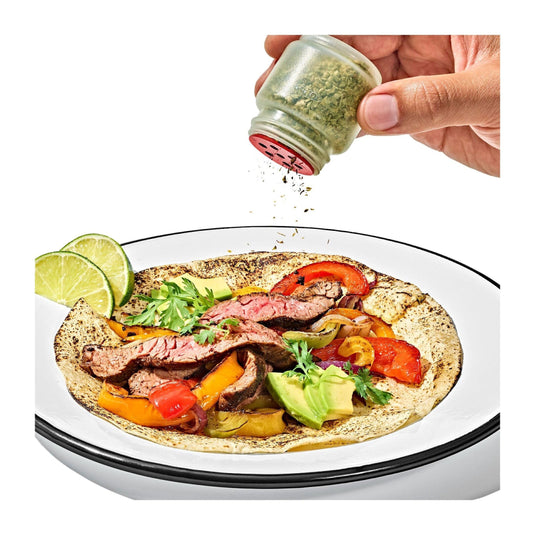 Hand sprinkling seasoning over a tortilla with meat and vegetables on a white plate.