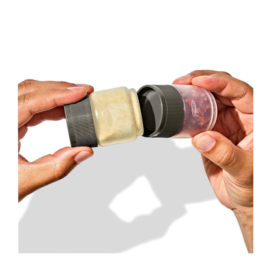 Two hands holding a spice grinder with a lid open, showing ground spices inside.