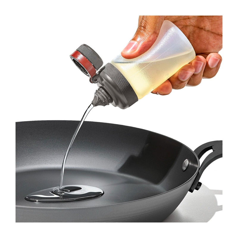 Load image into Gallery viewer, Hand pouring oil from a bottle into a frying pan on a white background
