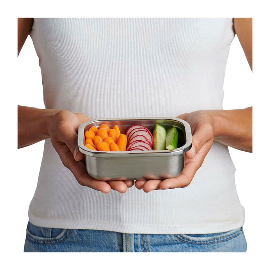 Person holding a metal lunch box with vegetables on a white background