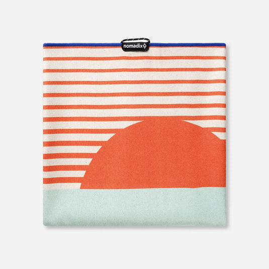 Folded fabric with orange and white stripes and a large orange circle on a light blue background, featuring the brand 'nomadix'.