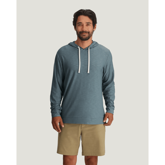 Man wearing a blue hoodie and beige shorts on a light gray background
