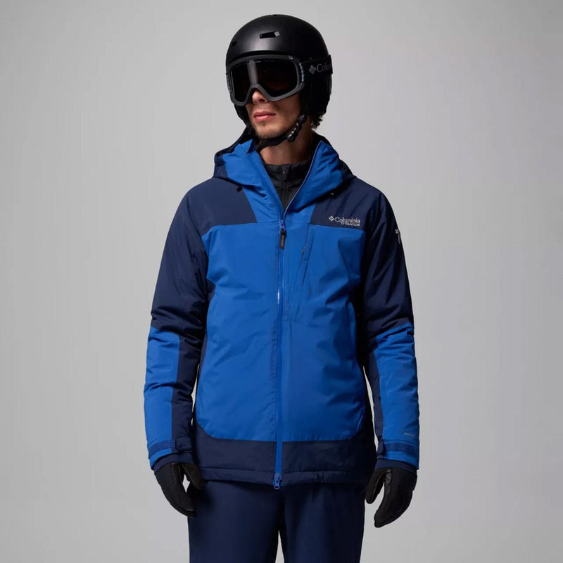 Load image into Gallery viewer, Person wearing a blue and navy ski jacket with a helmet and goggles on a gray background
