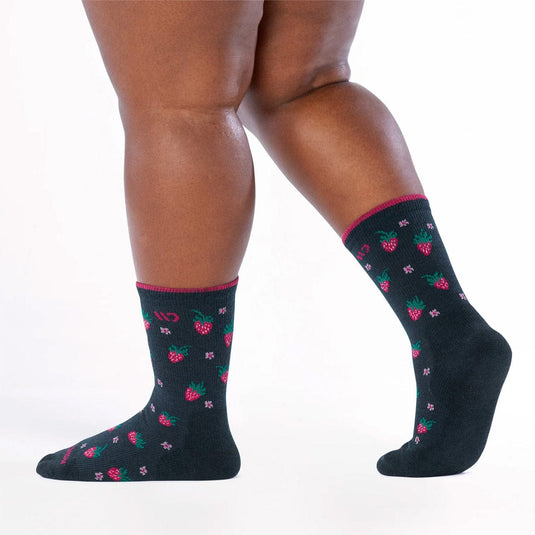 Black socks with pink and green patterns worn by a person on a white background