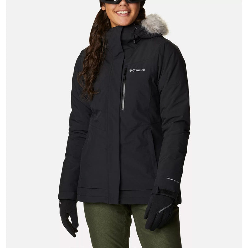 Load image into Gallery viewer, A woman wearing a black Columbia branded insulated jacket with a hood featuring a removable faux fur trim, ski pass pocket, and standing in front of a white background.
