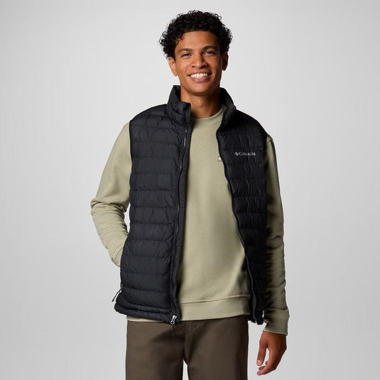Man wearing a black puffer vest over a green sweater on a white background