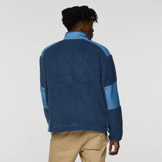 Person wearing a blue and gray pullover with beige pants on a white background