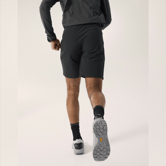 Person wearing black athletic shorts and shoes on a light gray background