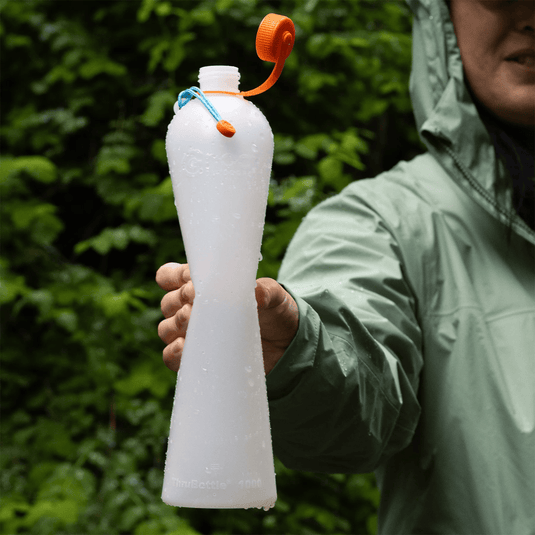 Person holding a white water bottle with an orange cap outdoors