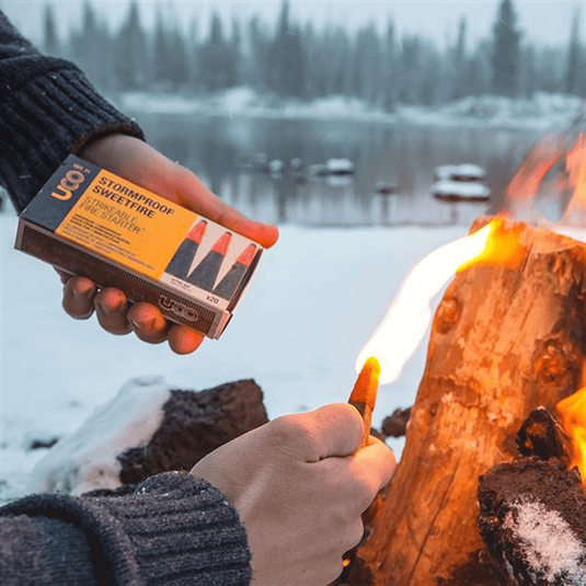 Person lighting a fire with Stormproof Sweetfire matches in a snowy landscape.