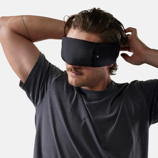 Man wearing a black sleep mask against a white background