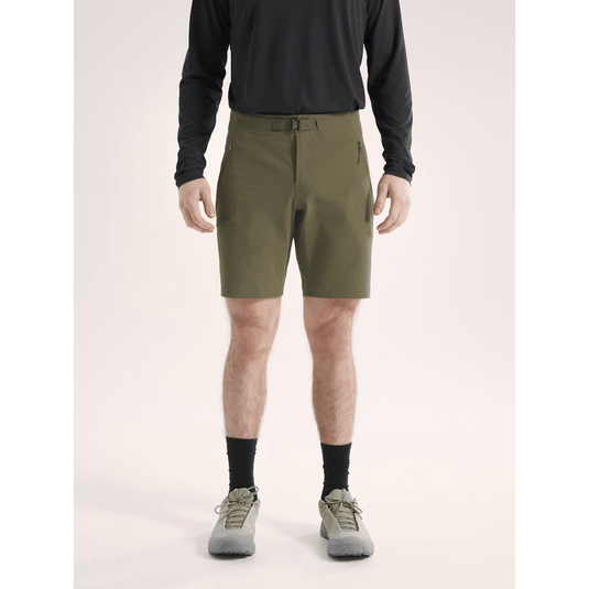 Person wearing olive green shorts with a black long-sleeve shirt on a light pink background