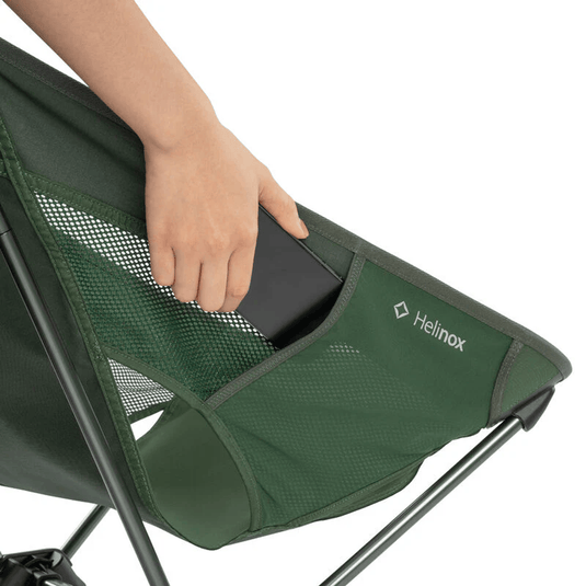 Green camping chair with a person's hand holding a phone, featuring the Helinox logo.