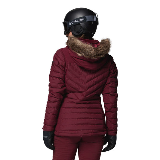 Person wearing a maroon winter jacket with fur hood and Columbia helmet on a white background