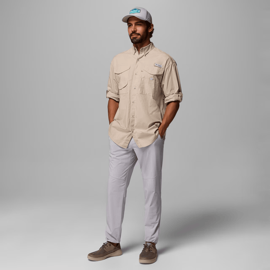 Man wearing a beige shirt and light gray pants with a cap on a gray background