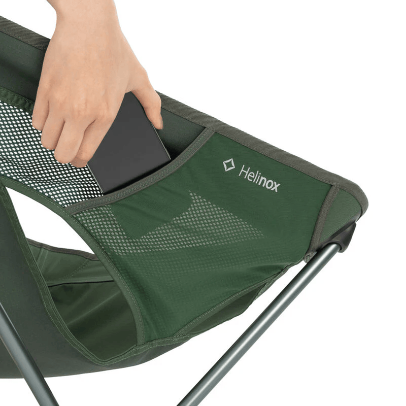Load image into Gallery viewer, Green camping chair with a hand placing an item into a pocket, featuring the Helinox logo.
