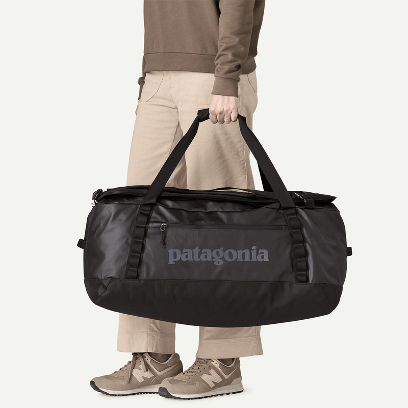 Load image into Gallery viewer, Person holding a black Patagonia duffel bag on a white background
