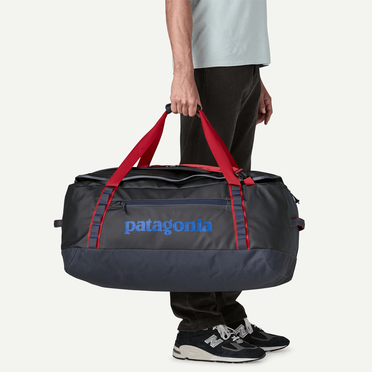 Person holding a Patagonia duffel bag with red straps on a white background